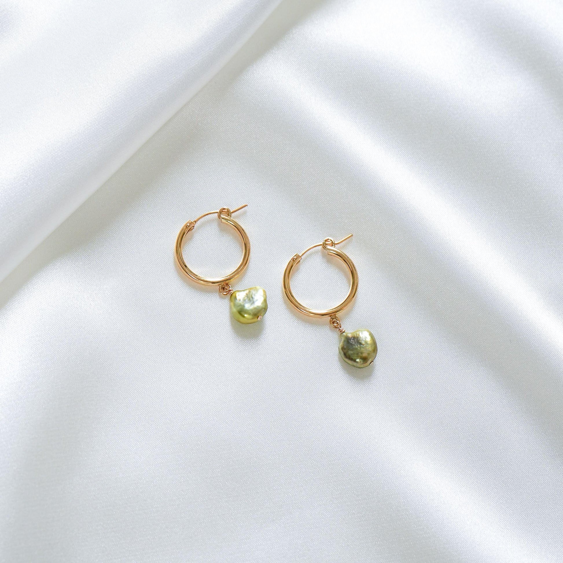 Gold hoop earrings with green keshi pearls on a white surface