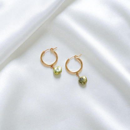 Gold hoop earrings with green keshi pearls on a white surface
