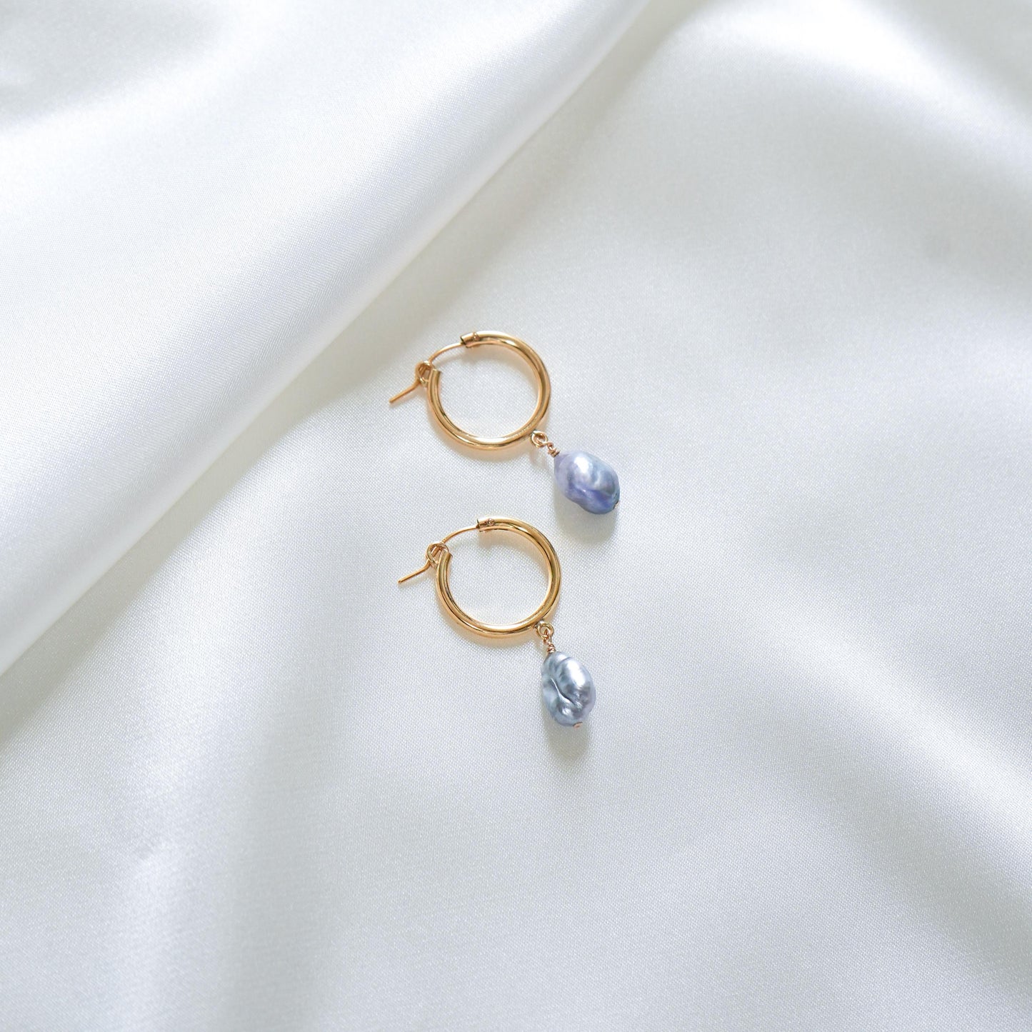 Gold hoop earrings with blue keshi pearl charms on a white surface