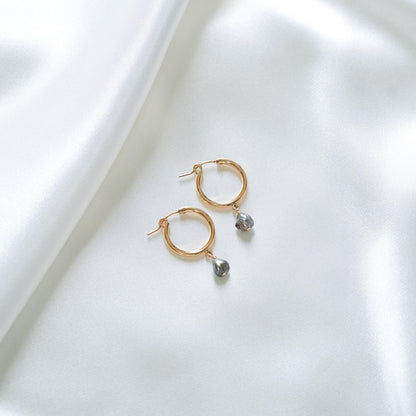 Gold hoop earrings with tahitian pearls on a white fabric background