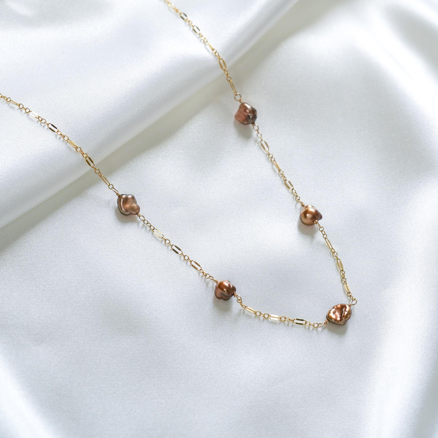 Gold necklace with brown keshi pearls on a white background