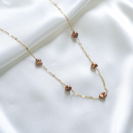 Gold necklace with brown keshi pearls on a white background