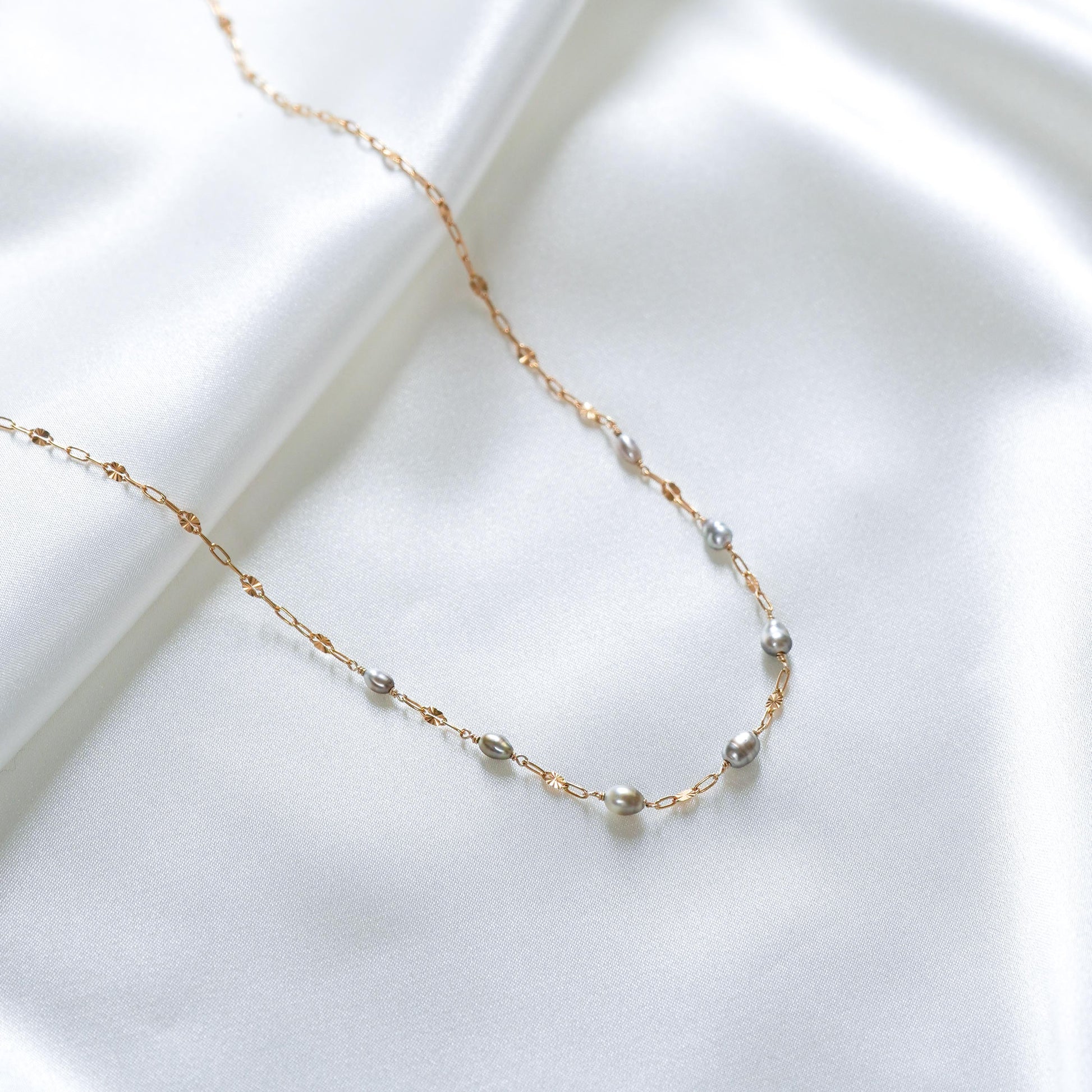 Delicate gold necklace with small pearl beads on a white surface