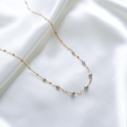 Delicate gold necklace with small pearl beads on a white surface