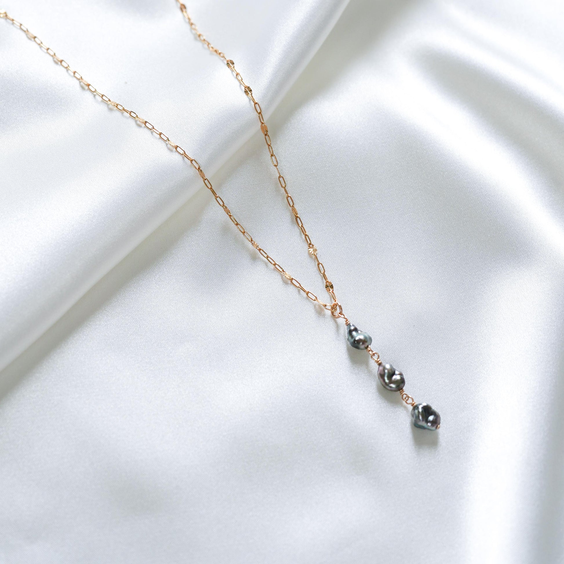 Necklace with three keshi beads on a gold chain against a white fabric background
