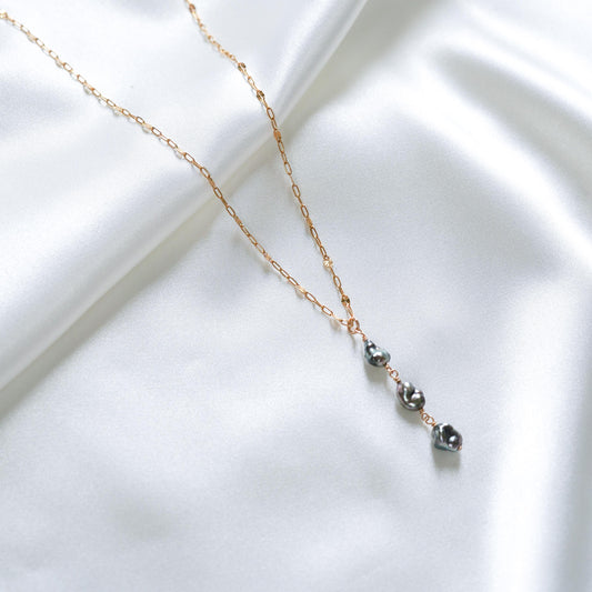 Necklace with three keshi beads on a gold chain against a white fabric background