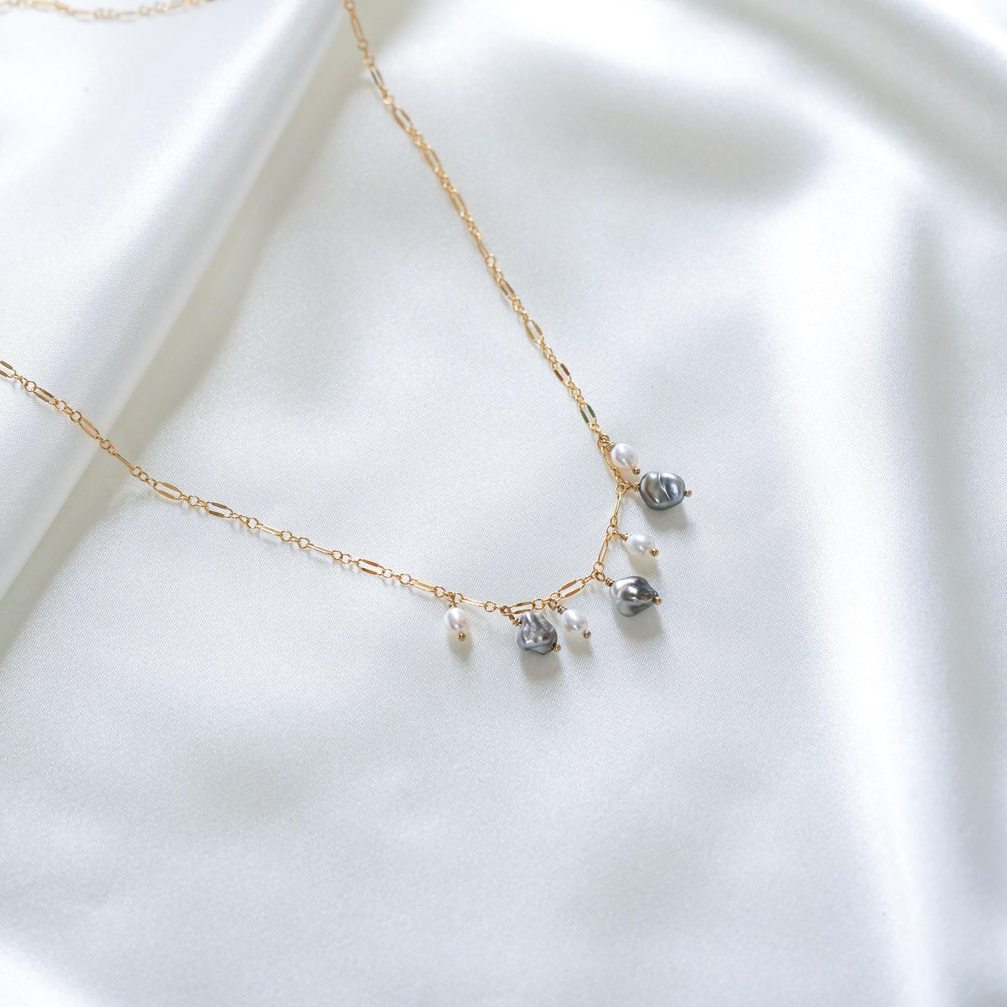 Delicate gold necklace with three white pearls and three keshi pearls on a white fabric background