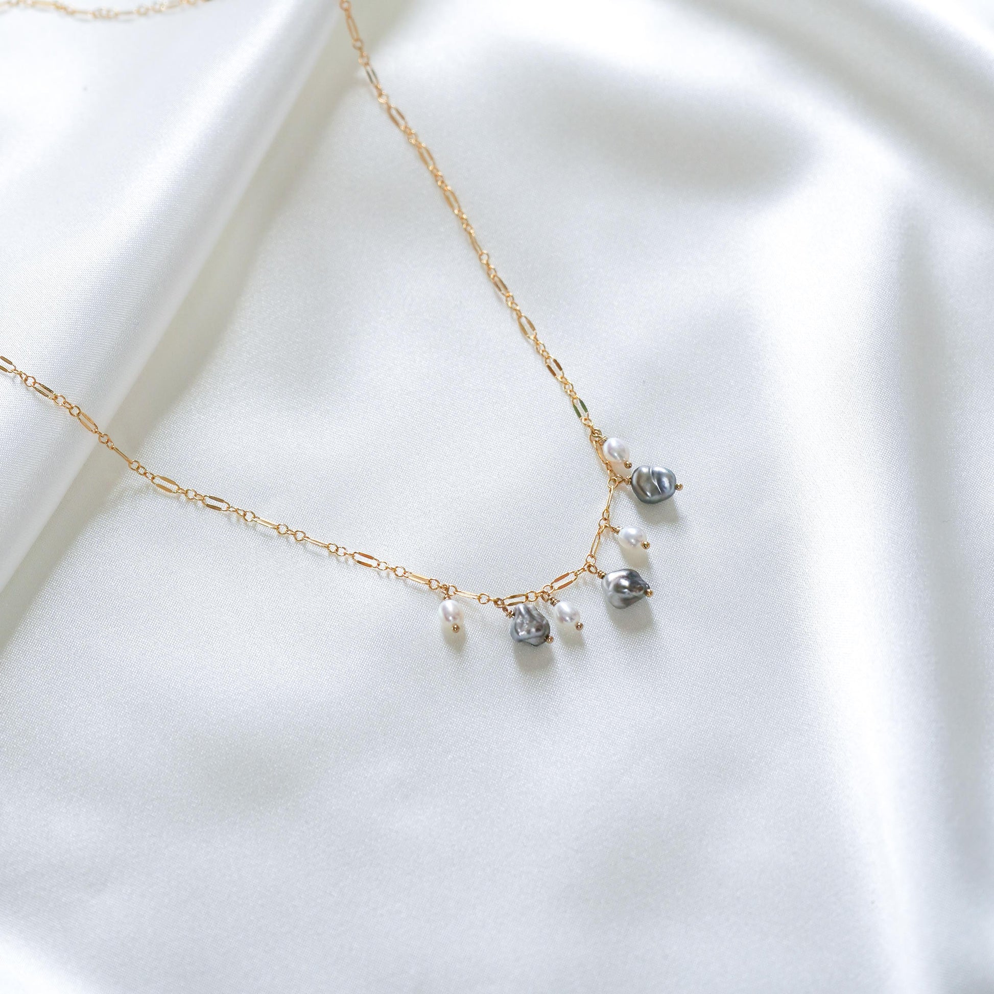 Delicate gold necklace with three white pearls and three keshi pearls on a white fabric background