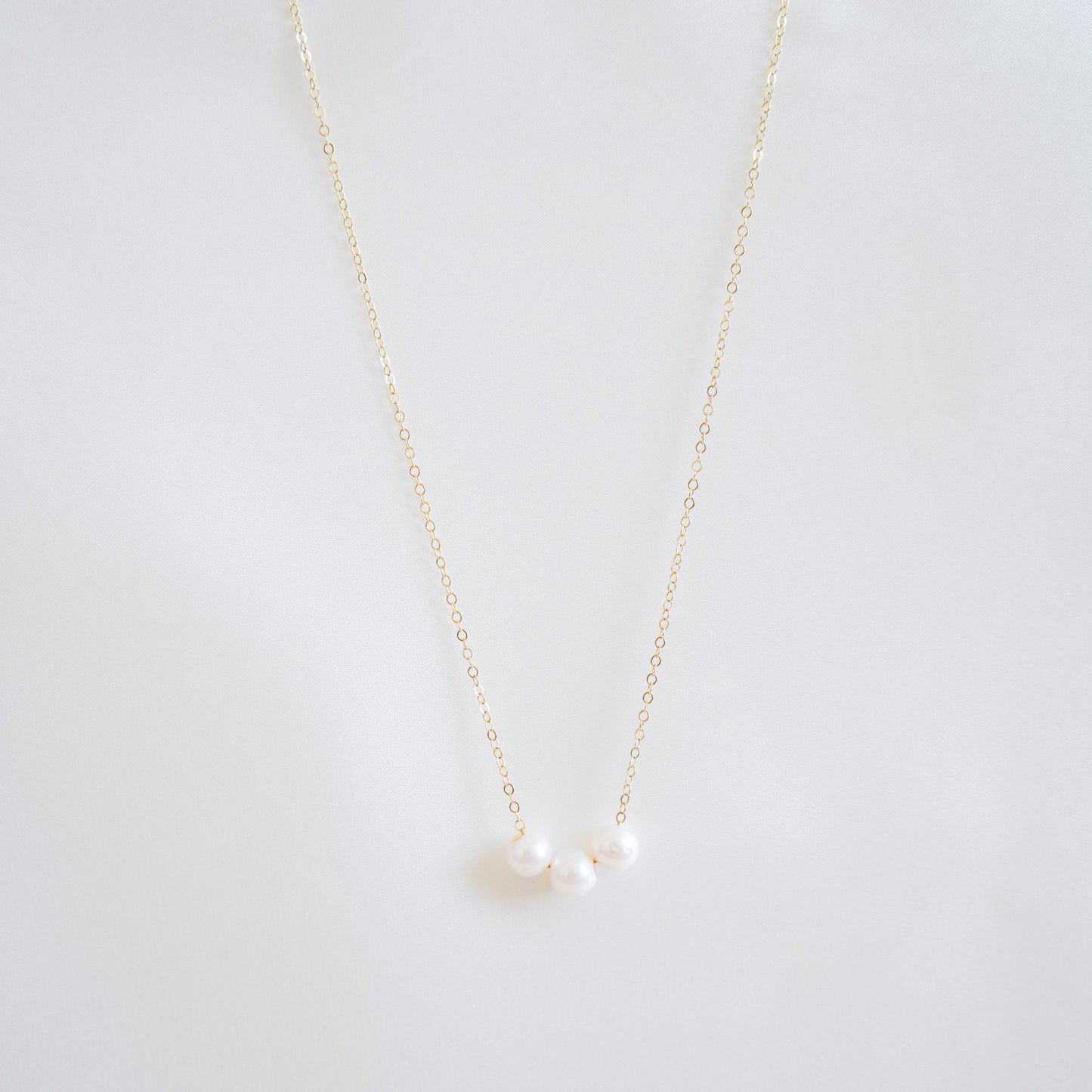 Gold necklace with three pearls on a white background