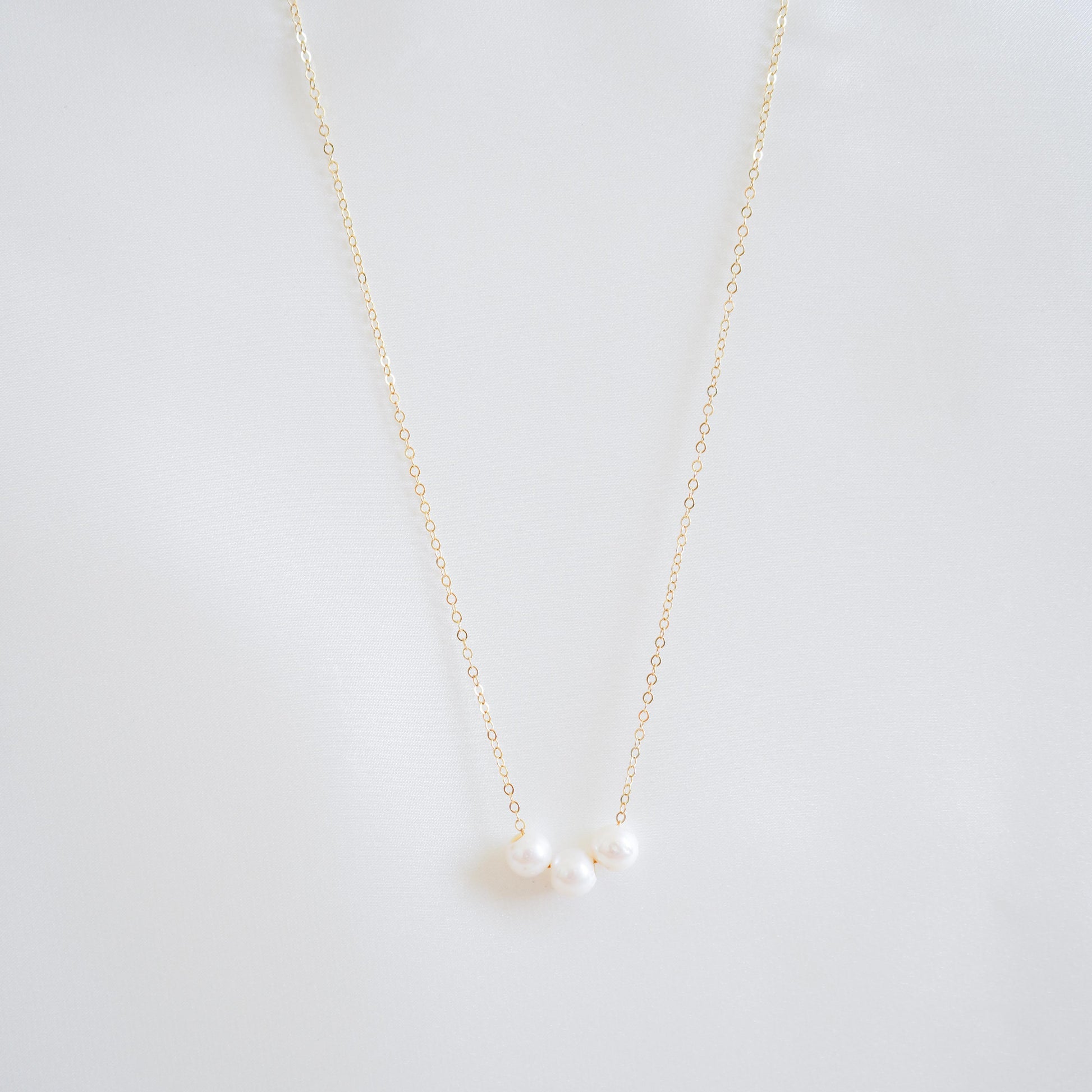 Gold necklace with three pearls on a white background
