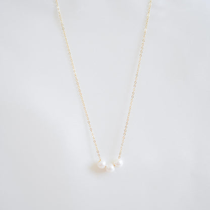 Gold necklace with three pearls on a white background