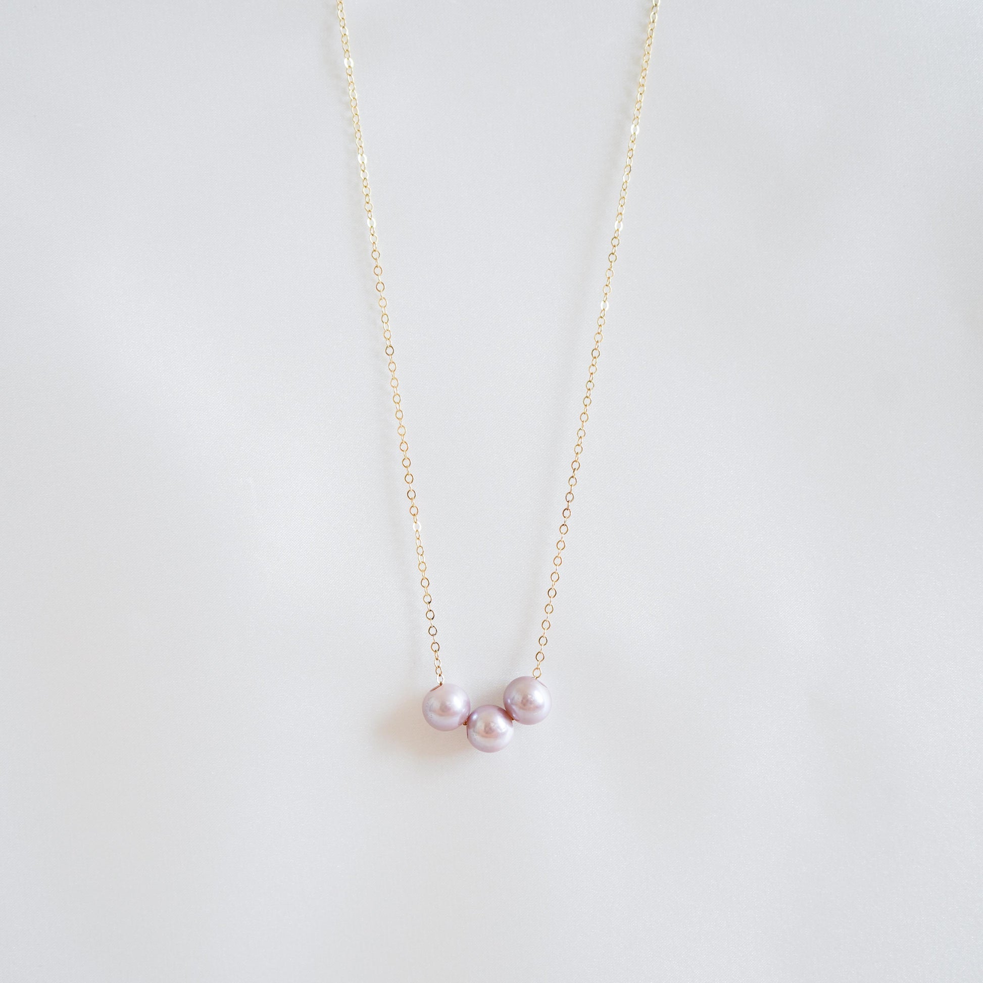 Pink pearl necklace on a thin chain against a light gray background