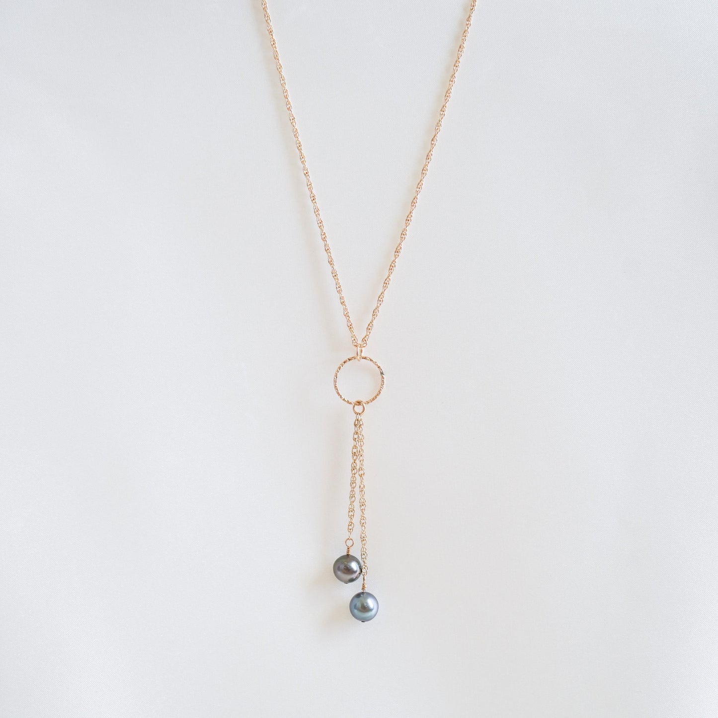 Gold necklace with circle charm and pearl pendants on a white background