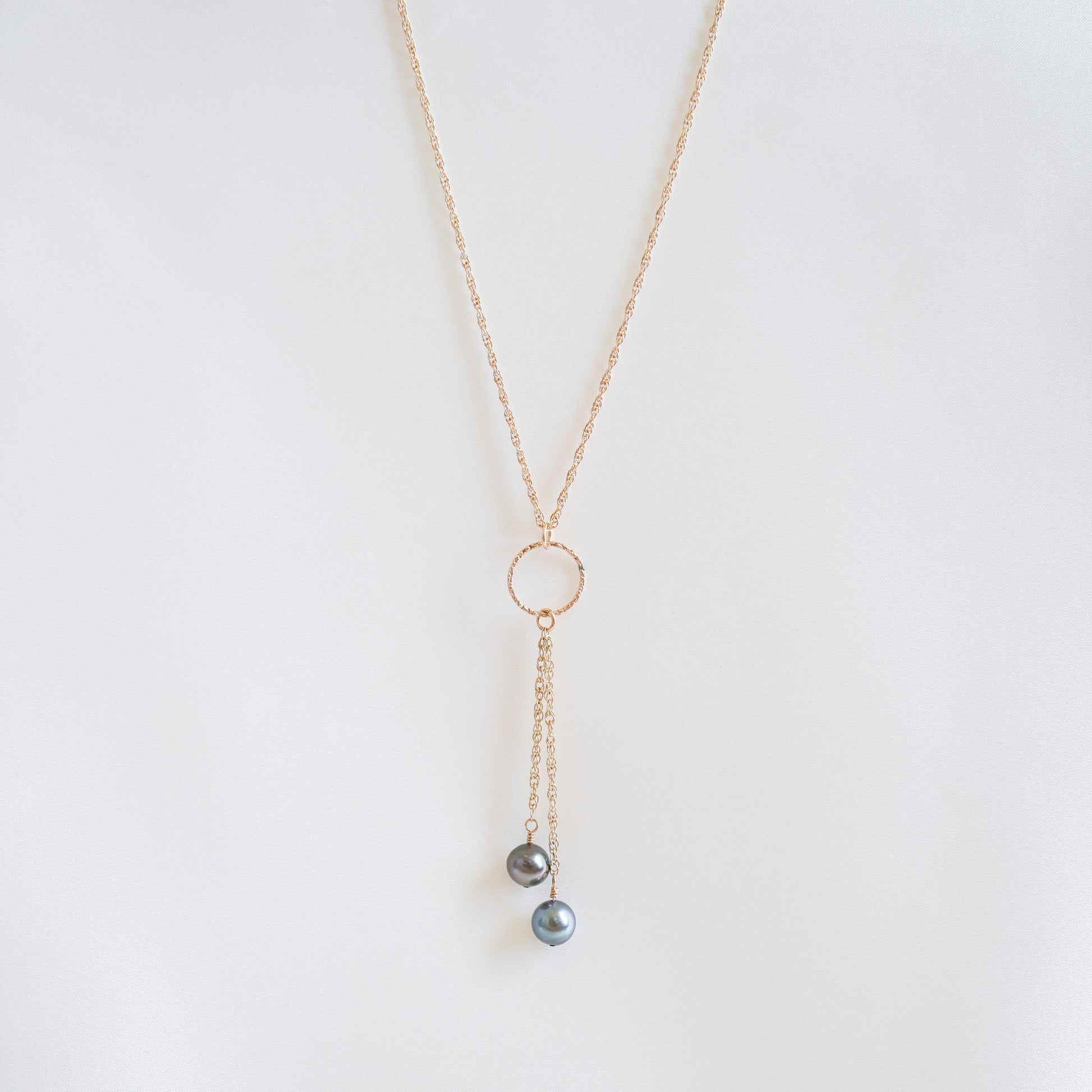 Gold necklace with circle charm and pearl pendants on a white background