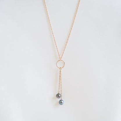 Gold necklace with circle charm and pearl pendants on a white background