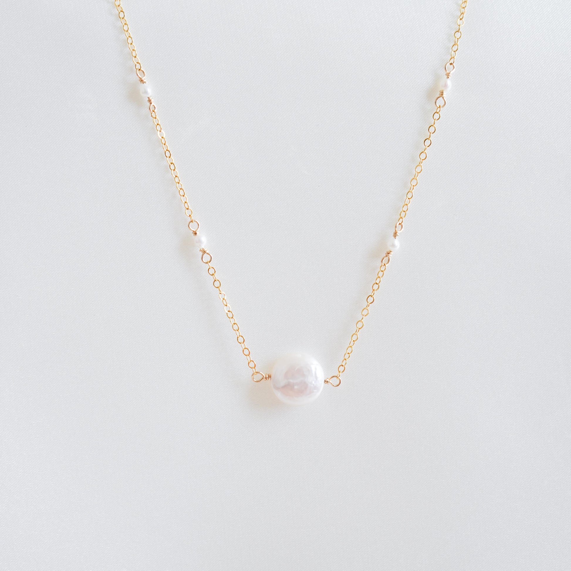 Gold necklace with a single coin pearl with smaller white pearls on a white background
