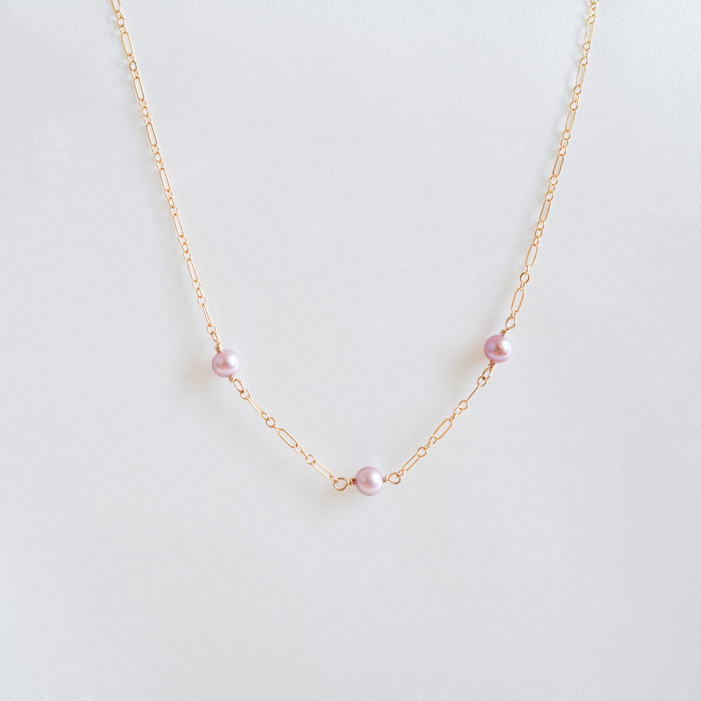 Gold necklace with pink pearls on a white background