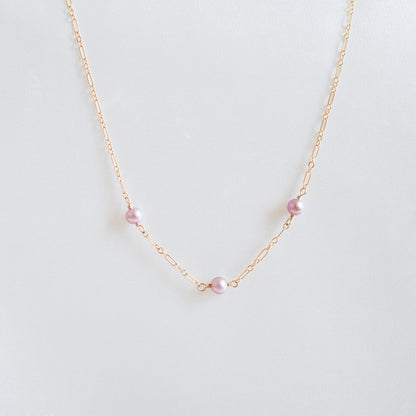 Gold necklace with pink pearls on a white background