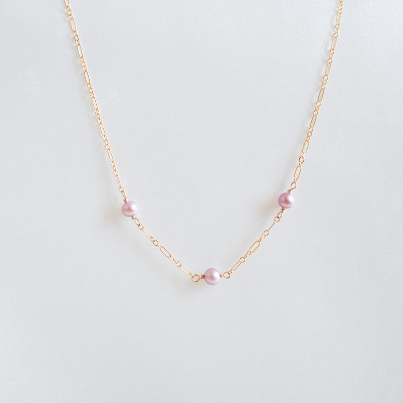 Gold necklace with pink pearls on a white background