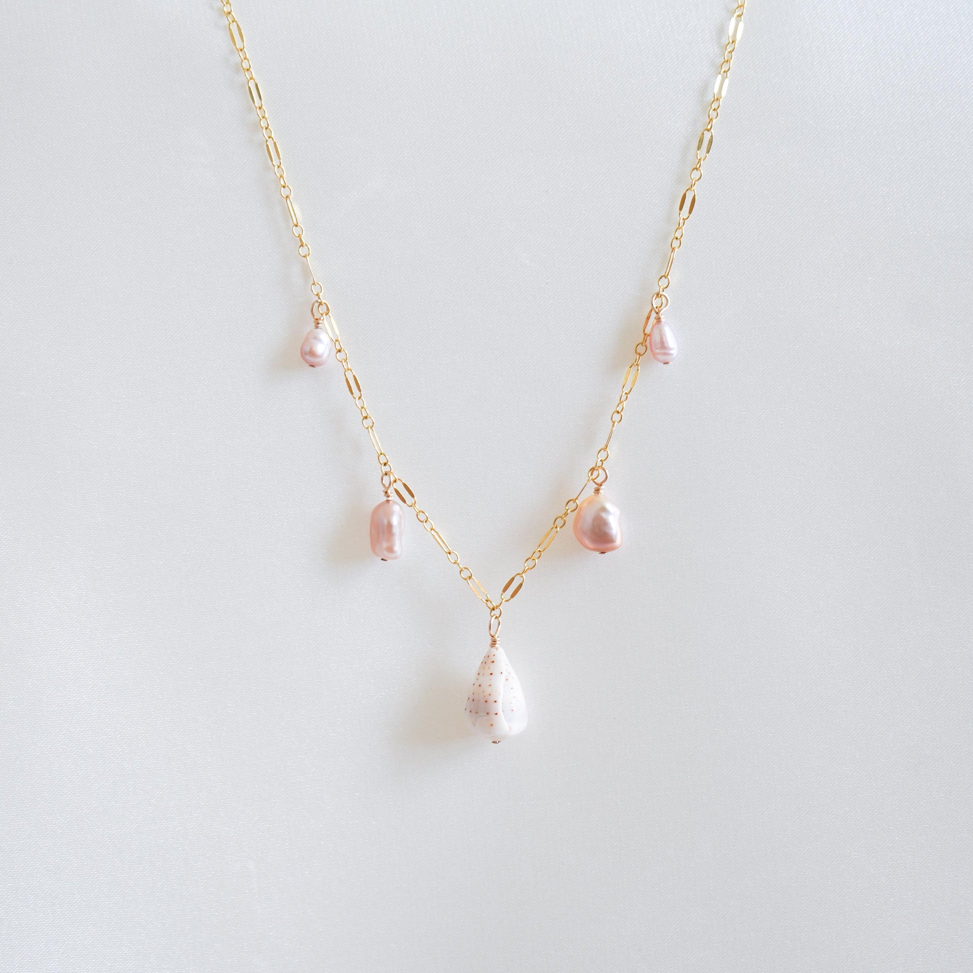 Necklace wit dangling pink pearls and white cone shell on gold chain