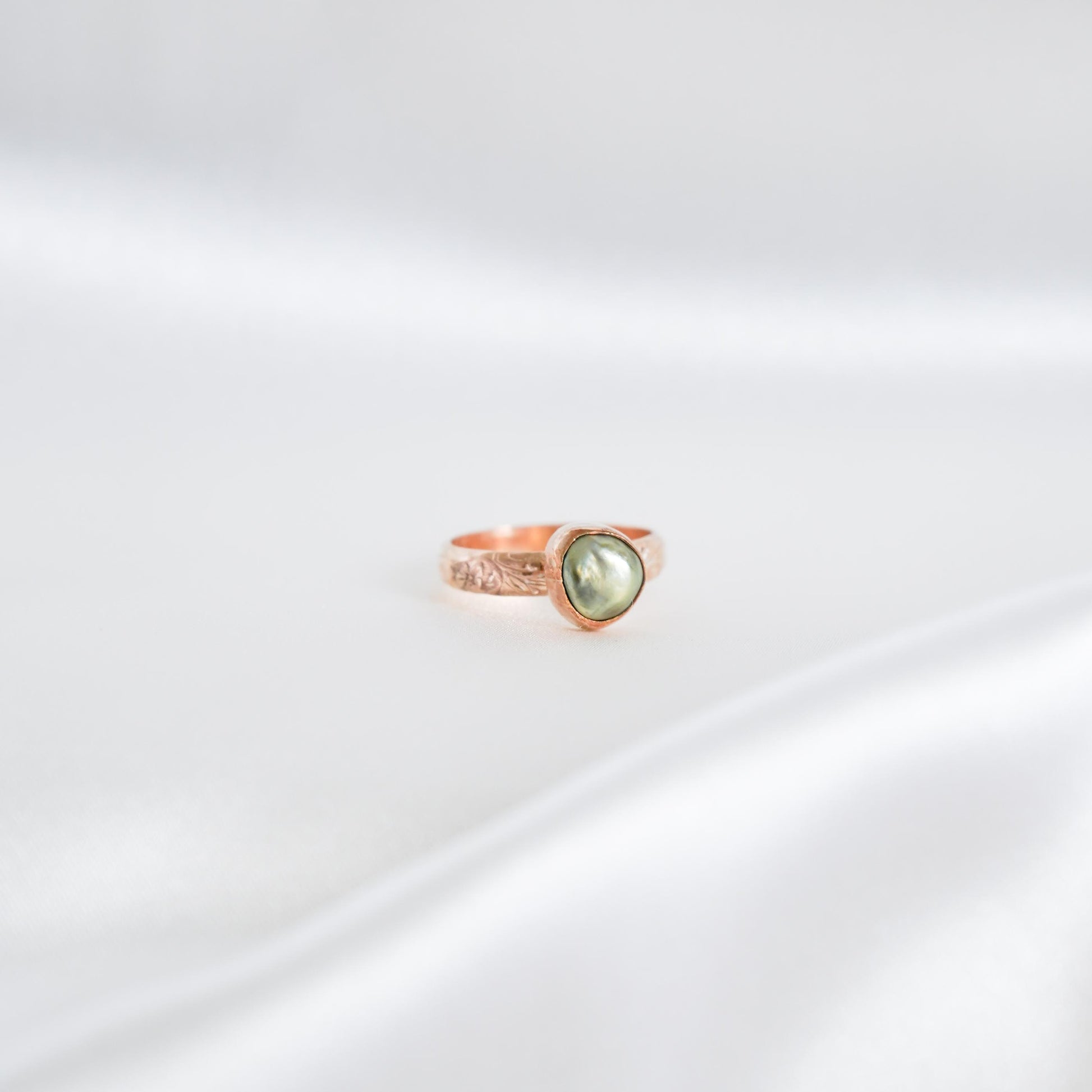 Gold ring with a green keshi pearl on a white background