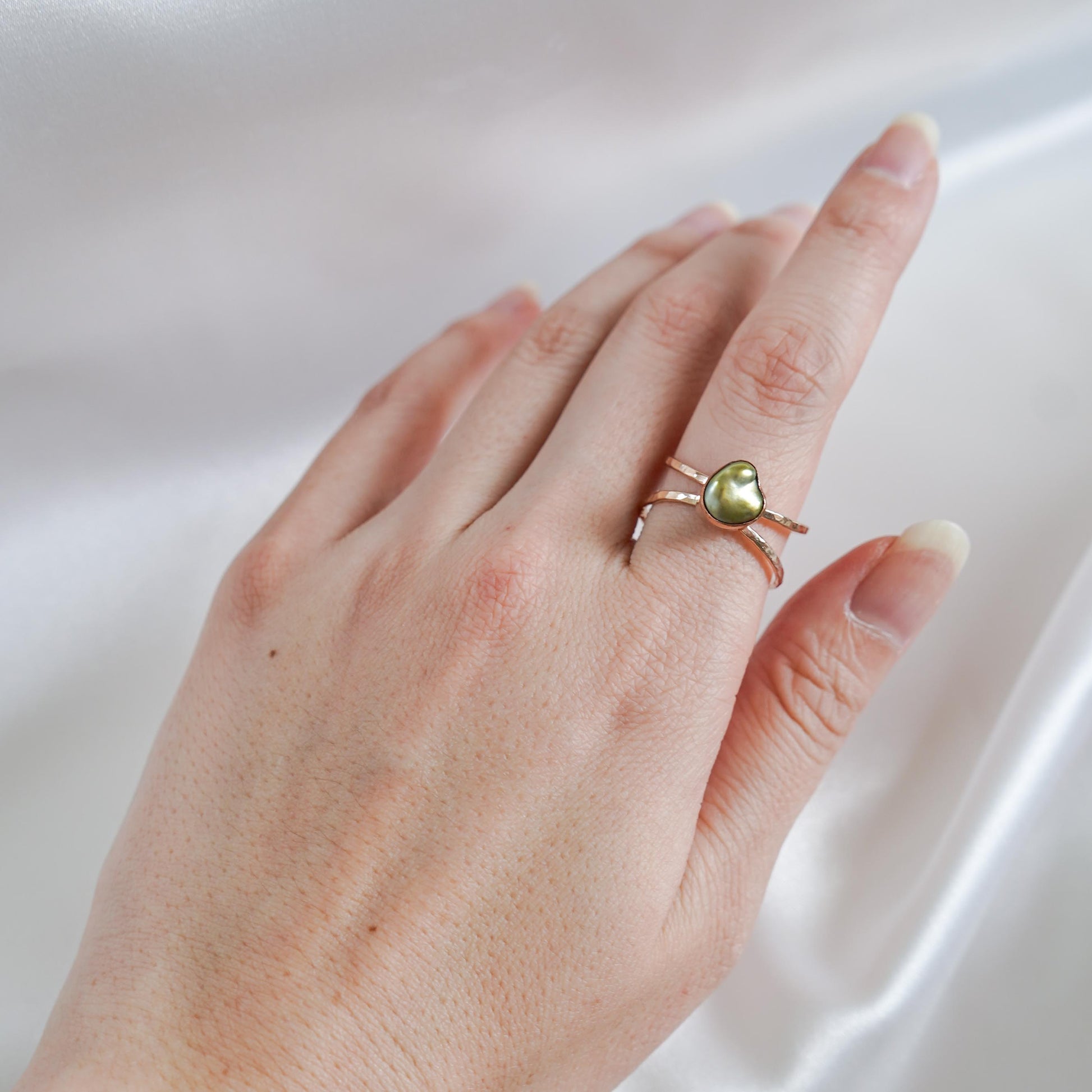 Hand wearing a ring with a green keshi pearl on a white background
