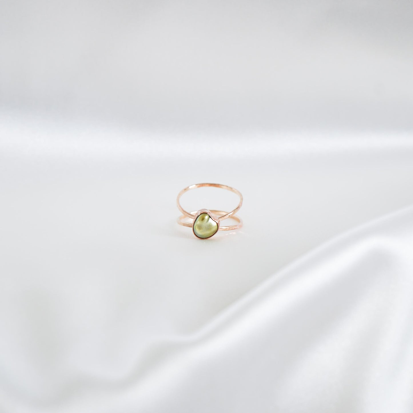 Gold ring with a green keshi pearl on a white satin background