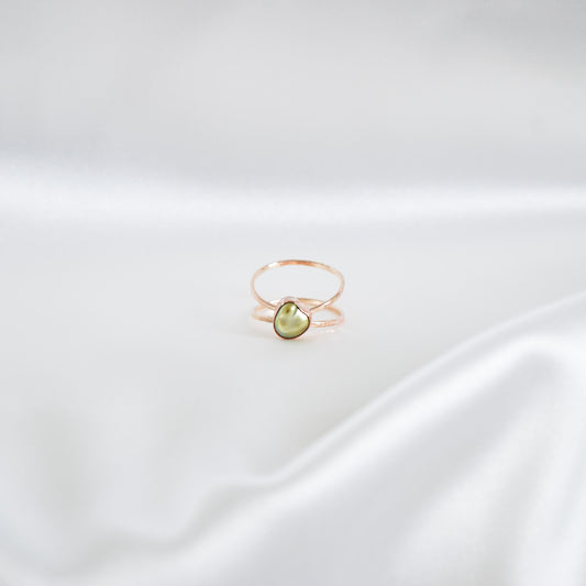 Gold ring with a green keshi pearl on a white satin background