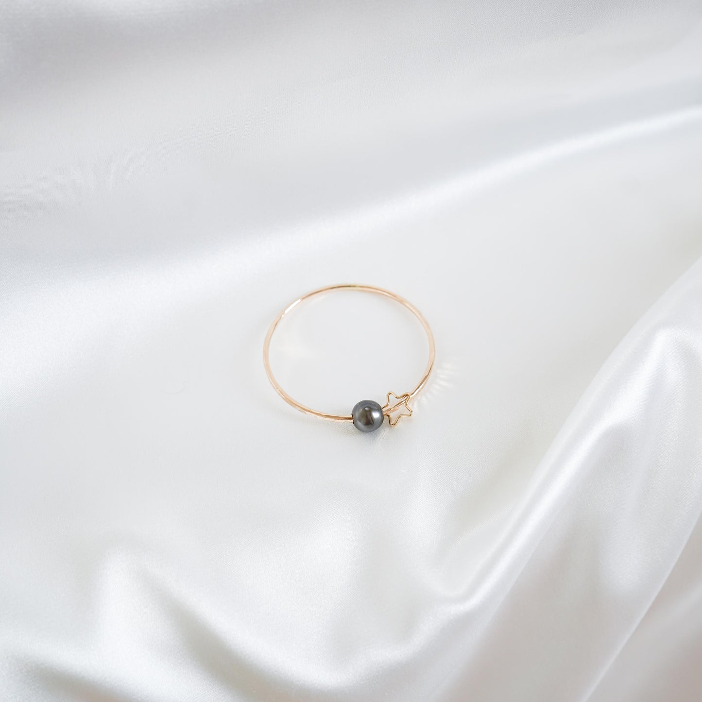Gold bracelet with a single pearl and star charm on a white background