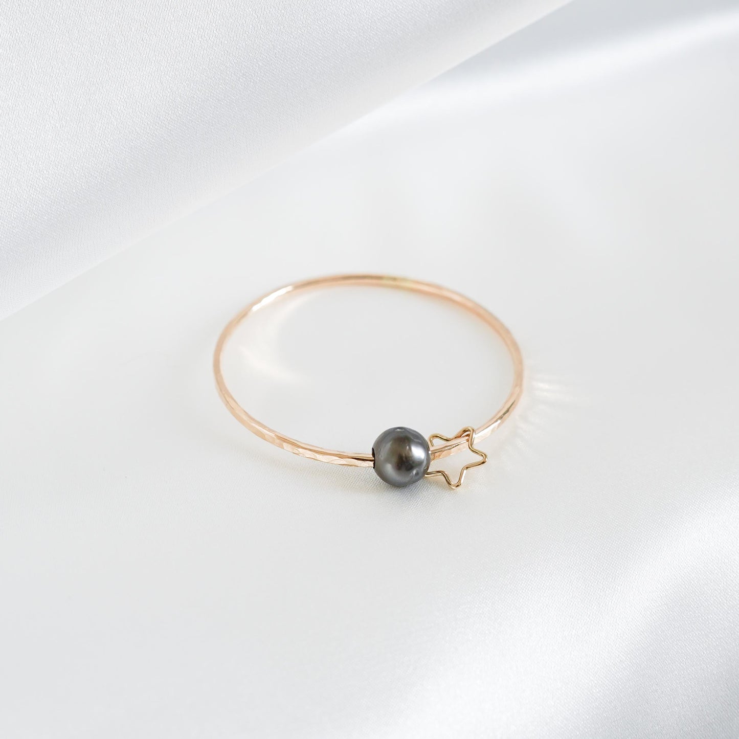Gold bracelet with a single pearl and star charm on a white background