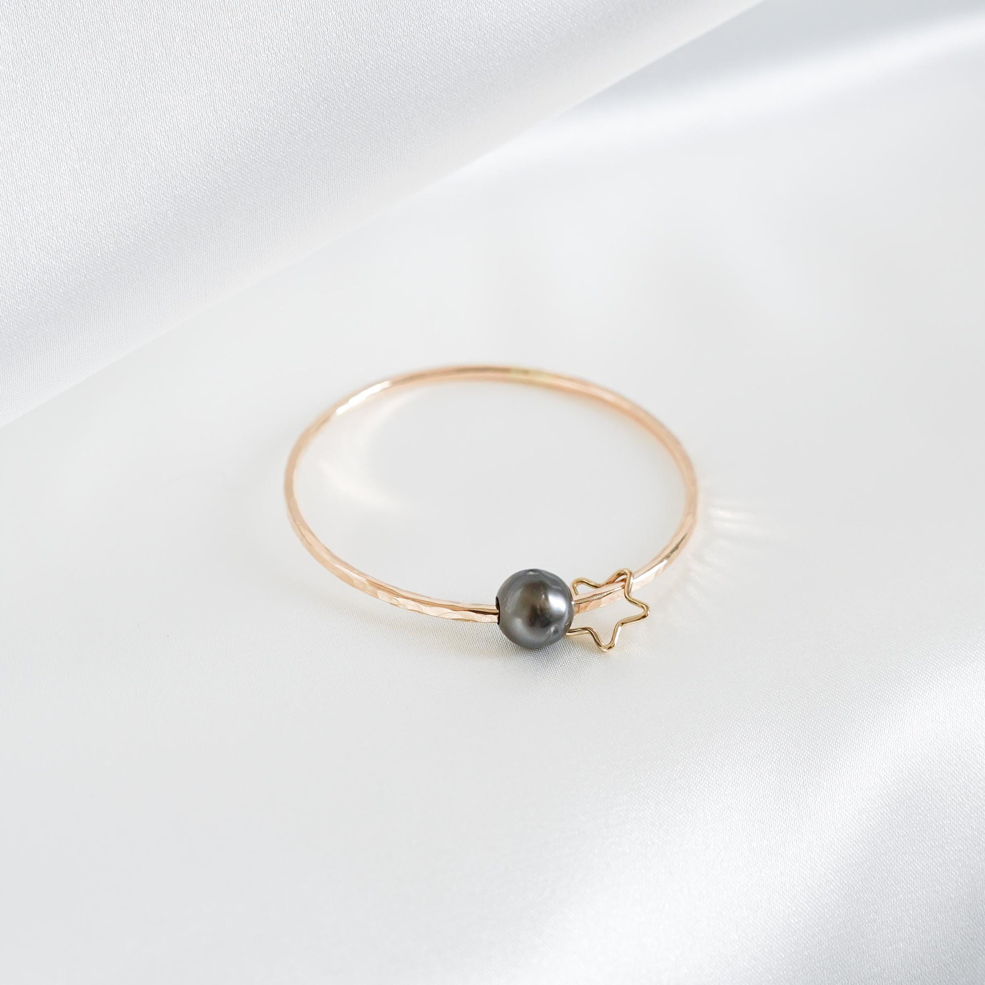 Gold bracelet with a single pearl and star charm on a white background