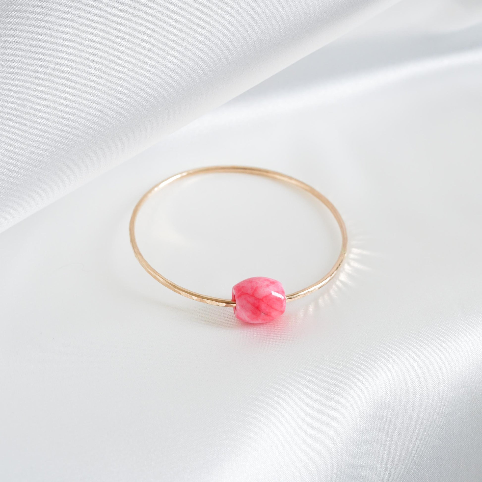 Gold bracelet with a pink jade bead on a white background