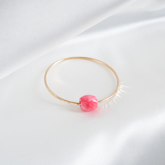 Gold bracelet with a pink jade bead on a white background