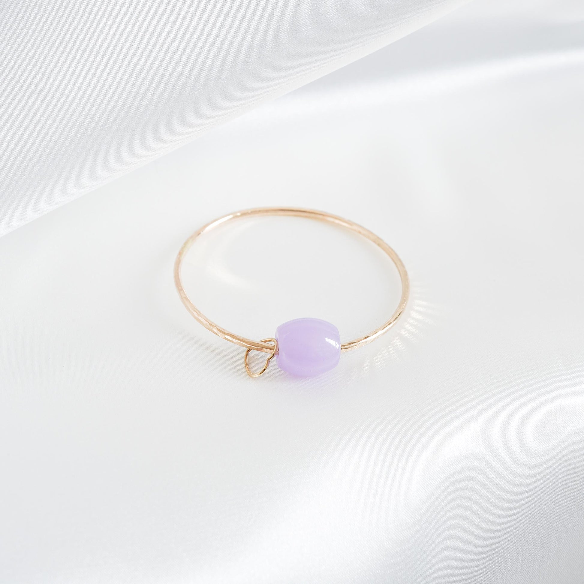 Gold bracelet with a purple jade bead and heart charm on a white background