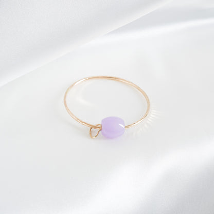 Gold bracelet with a purple jade bead and heart charm on a white background