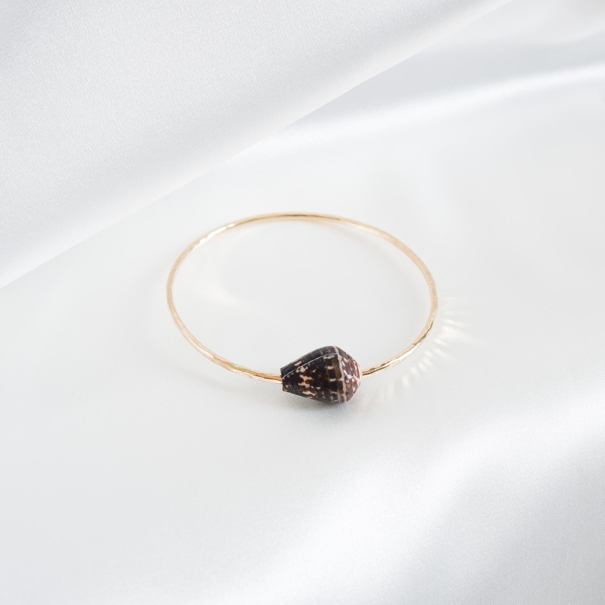 Gold bracelet with a black and white patterned shell on a white background