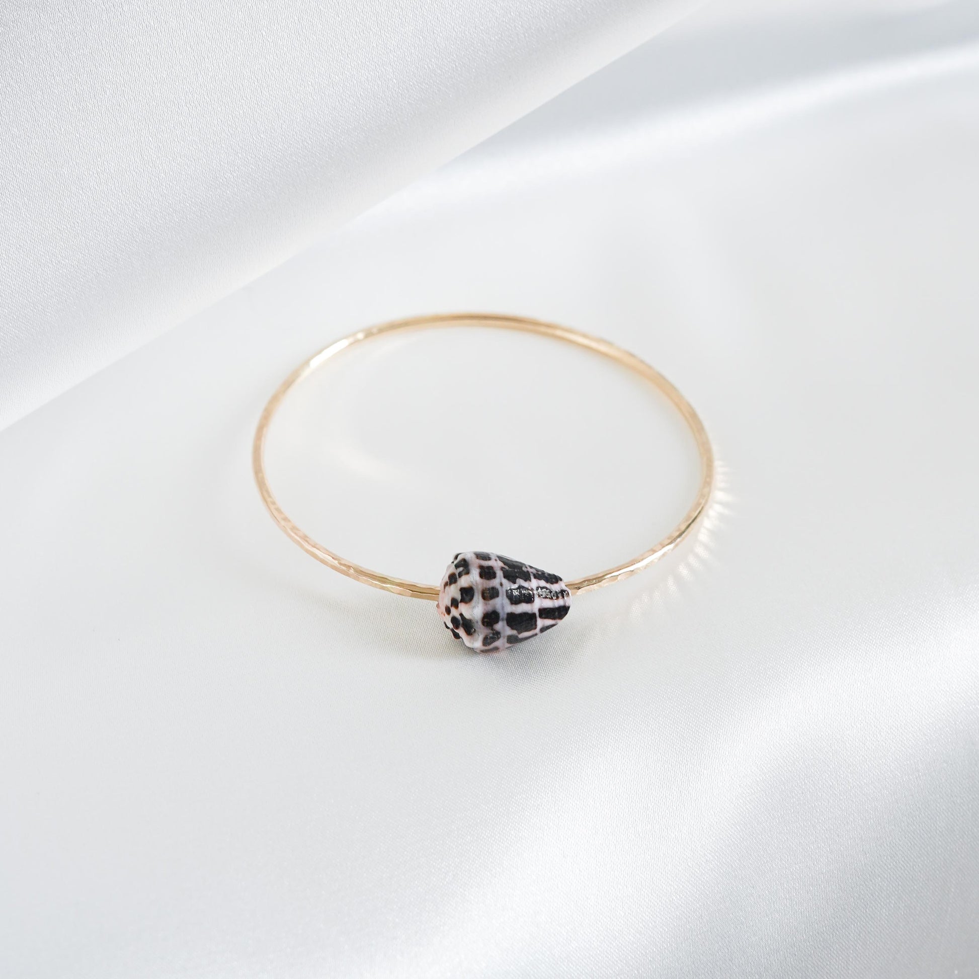 Gold bracelet with a black and white patterned shell on a white background
