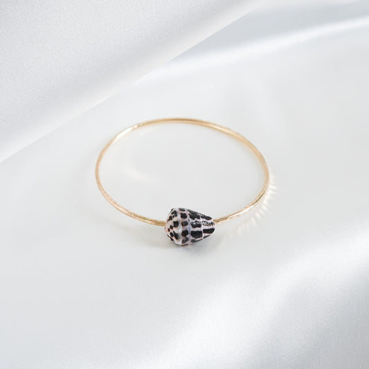 Gold bracelet with a black and white patterned shell on a white background