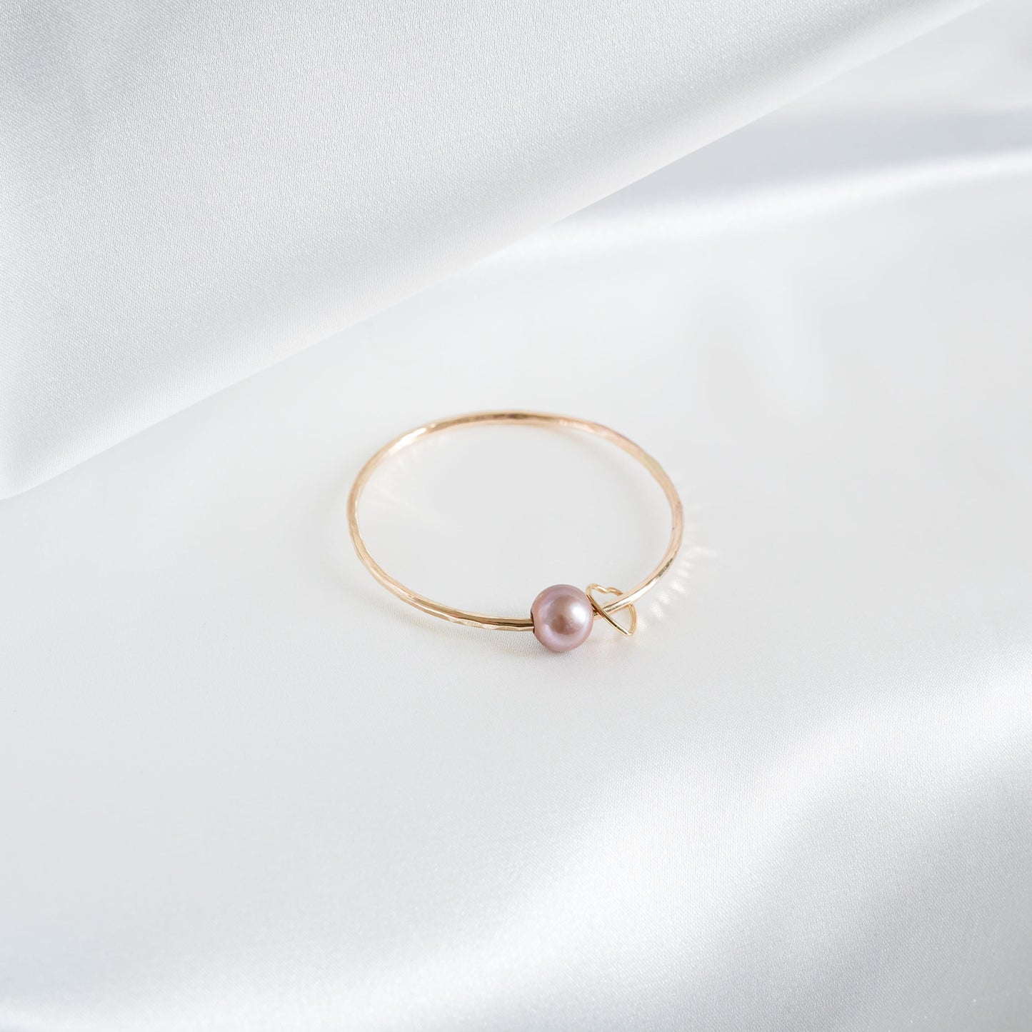 Gold bracelet with a single pearl and heart charm on a white background