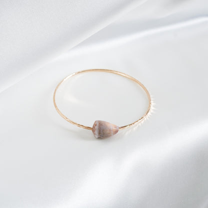 Gold bracelet with a light cone shell on a white background