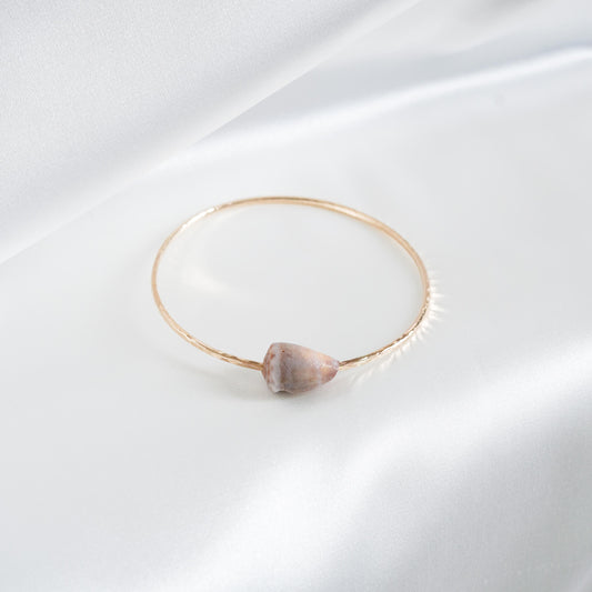 Gold bracelet with a light cone shell on a white background