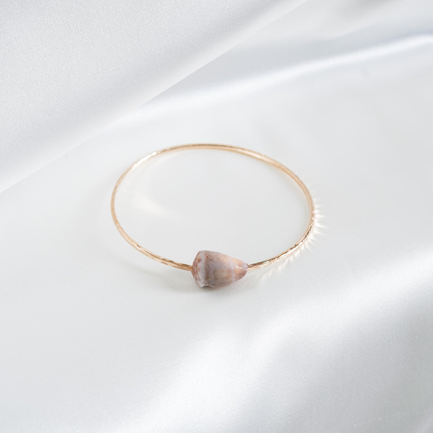 Gold bracelet with a tan shell on a white background