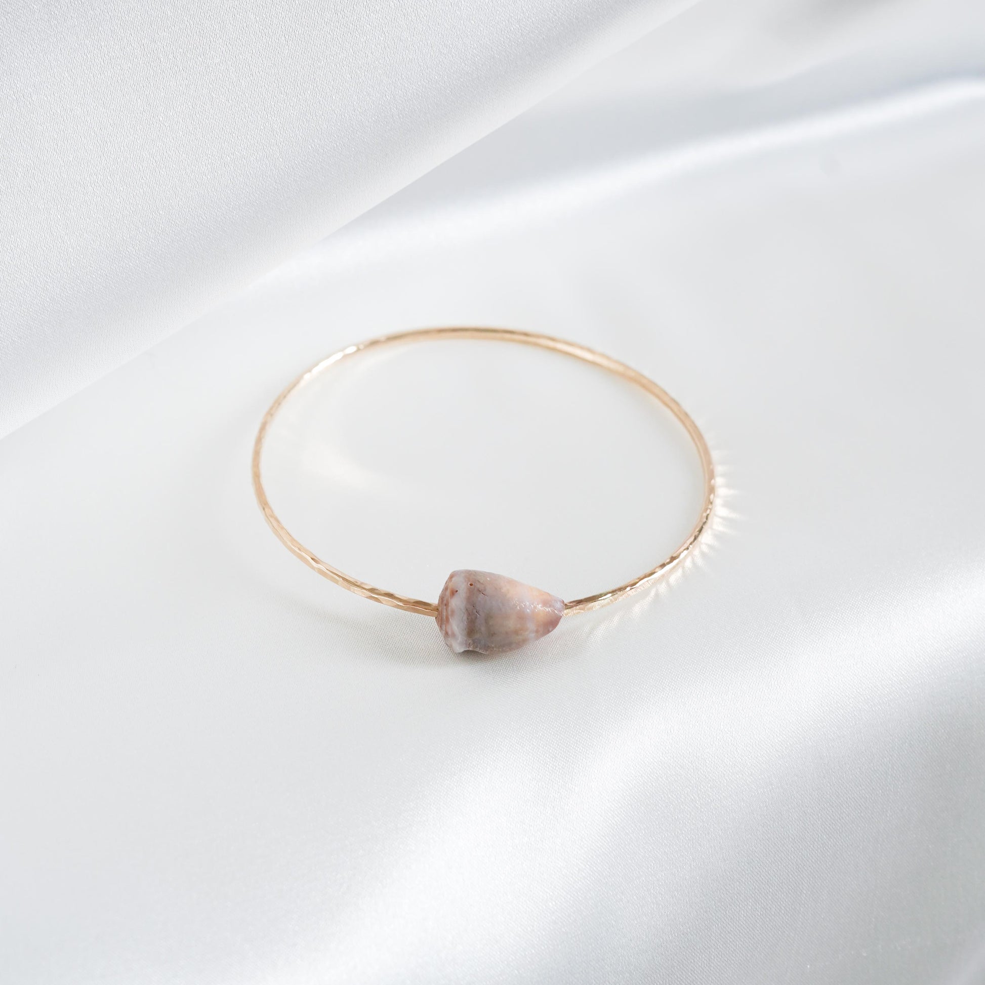 Gold bracelet with a tan shell on a white background