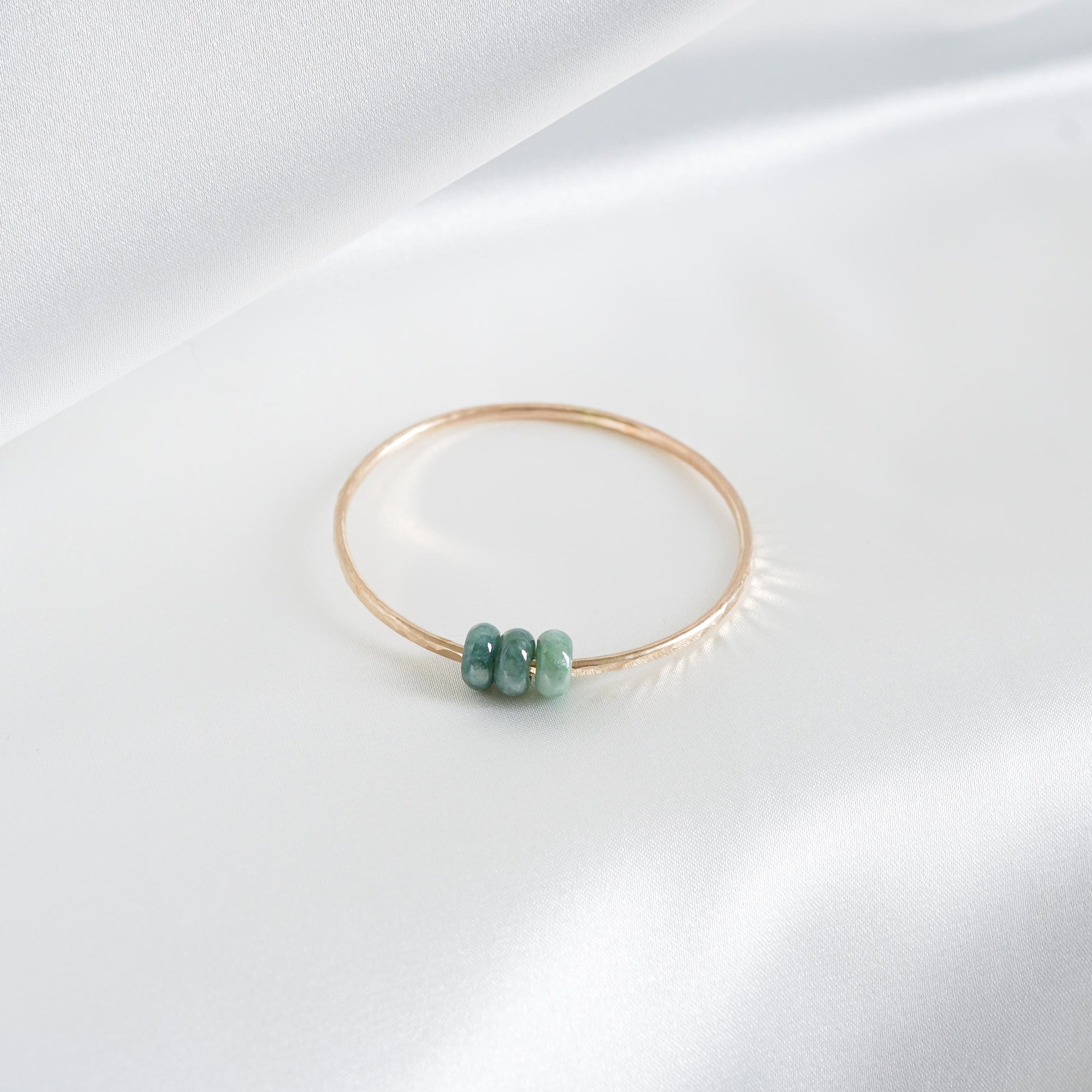 Gold bracelet with three green jade beads on a white background