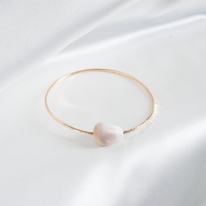Gold bracelet with a white shell on a white fabric background