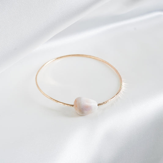 Gold bracelet with a white shell on a white fabric background
