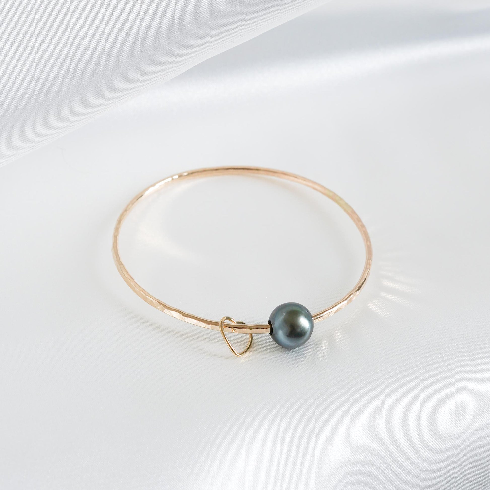 Gold bracelet with a single pearl and heart charm on a white background