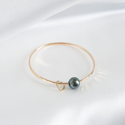 Gold bracelet with a single pearl and heart charm on a white background