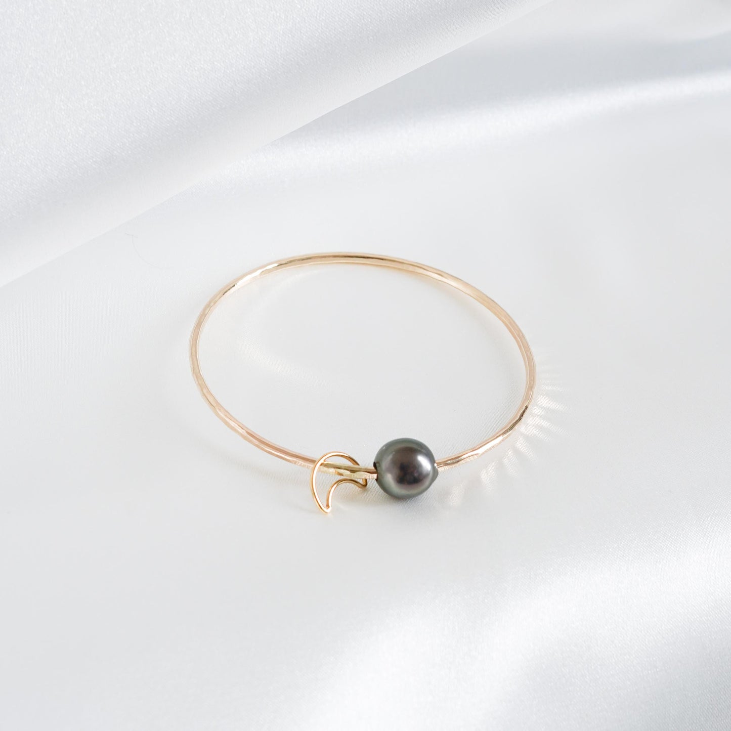 Gold bracelet with a single pearl and moon charm on a white background
