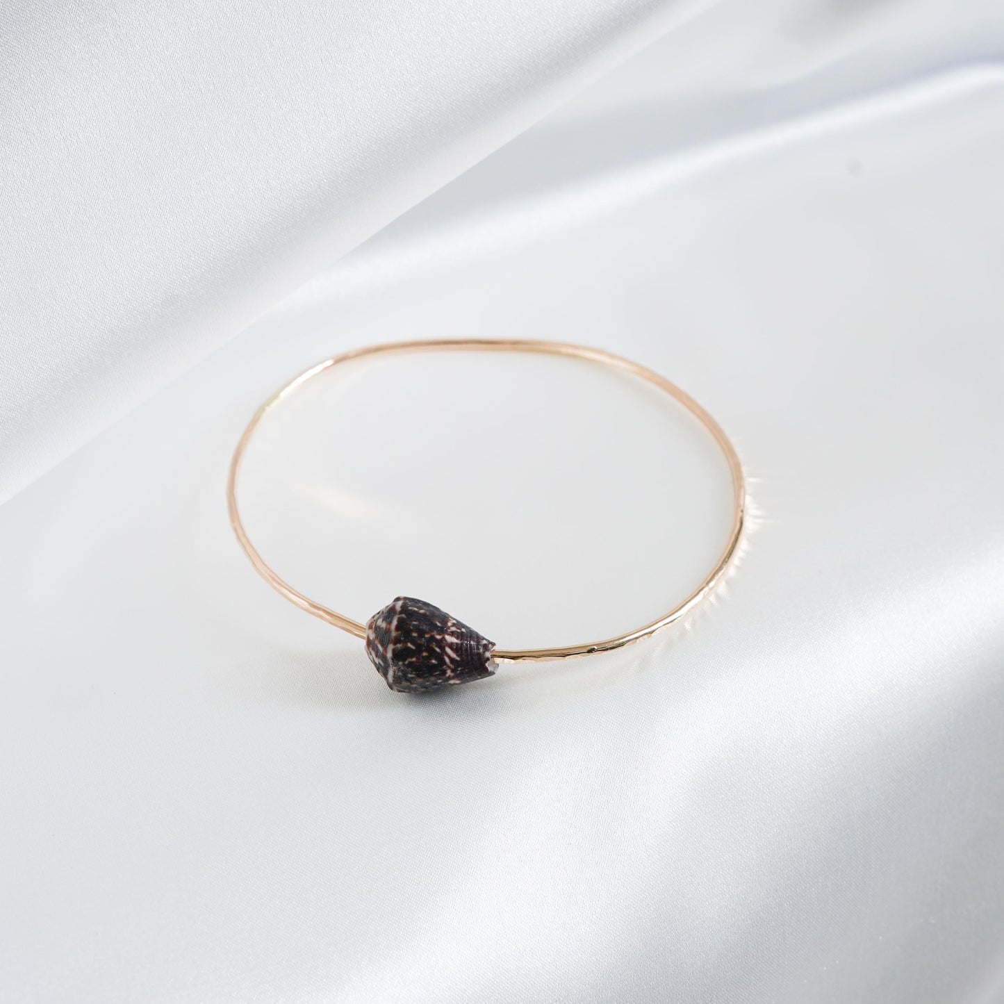 Gold bracelet with a dark shell on a white fabric background